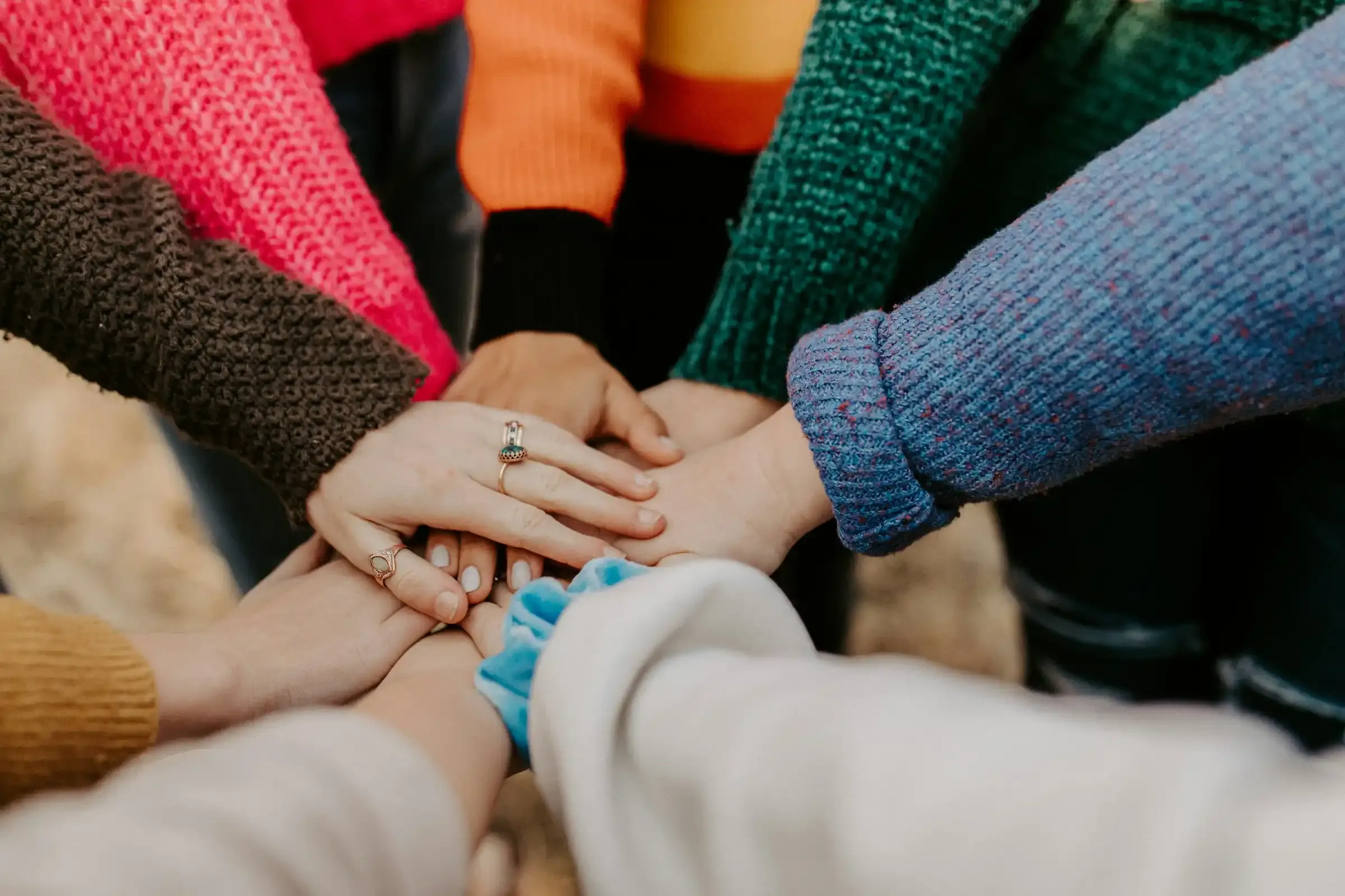 Mehrere Menschen stehen im Kreis und legen ihre Hände übereinander als Symbol für Teamwork.